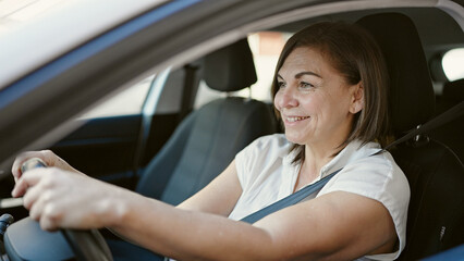 Middle age hispanic woman smiling confident driving car at street