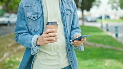 Young caucasian man using smartphone drinking coffee at park