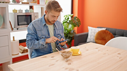 Young caucasian man using smartphone having breakfast at dinning room
