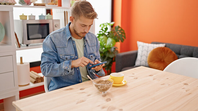 Young caucasian man using smartphone having breakfast at dinning room