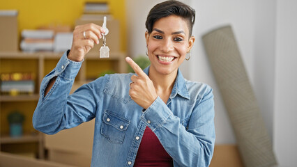 Young beautiful hispanic woman smiling confident pointing to key at new home