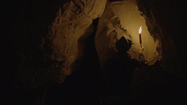 Male Adventurer Exploring Stone Rock Cave in Darkness Outside Using Torch Light
