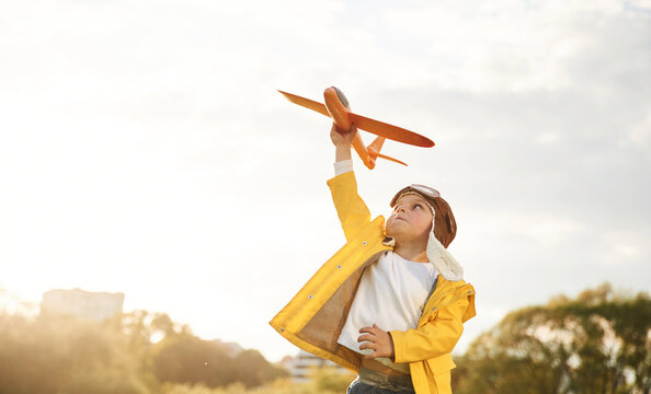 In Yellow Colored Jacket. Little Boy Is Playing With Toy Plane On The Summer Field