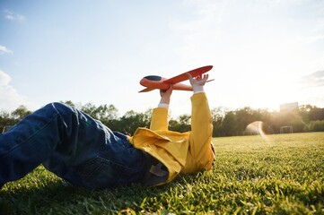Lying down on ground. Little boy is playing with toy plane on the summer field