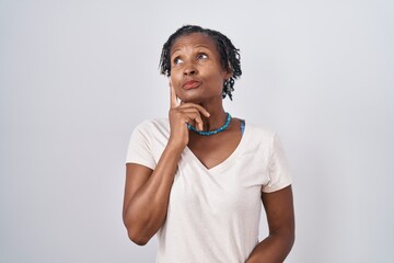 African woman with dreadlocks standing over white background with hand on chin thinking about question, pensive expression. smiling with thoughtful face. doubt concept.