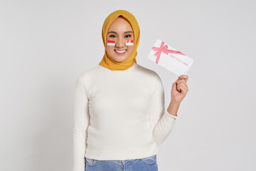 Smiling happy young Asian Muslim woman wearing a hijab holding a gift voucher certificate isolated...