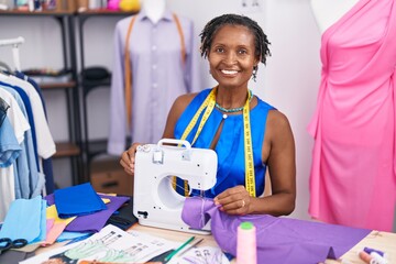Middle age african american woman tailor smiling confident using sewing machine at atelier