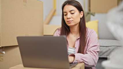 Young beautiful hispanic woman using laptop sitting on floor at new home