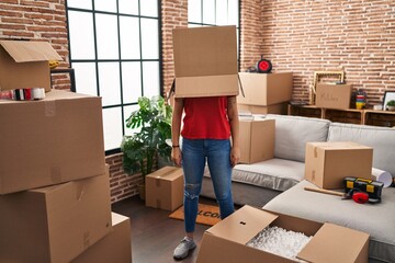 Young beautiful hispanic woman wearing cardboard box on head at new home