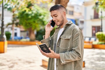 Young hispanic man talking on the smartphone reading passport at park