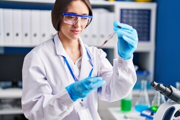 Young beautiful hispanic woman scientist pouring blood on test tube at laboratory
