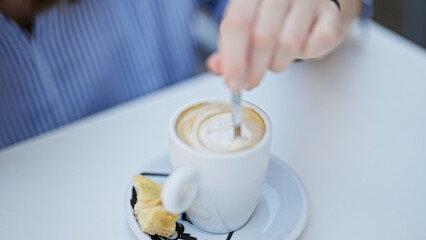 Young beautiful hispanic woman stir the coffee sitting on table at coffee shop terrace