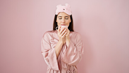 Young beautiful hispanic woman wearing sleep mask drinking cup of coffee over isolated pink background