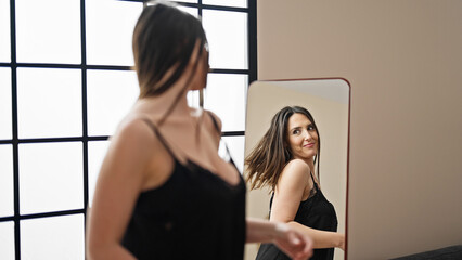 Young beautiful hispanic woman smiling confident looking herself on mirror at home