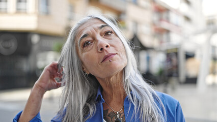 Middle age grey-haired woman standing with serious expression combing hair at street