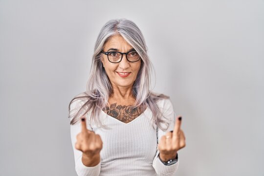 Middle age woman with grey hair standing over white background showing middle finger doing fuck you bad expression, provocation and rude attitude. screaming excited