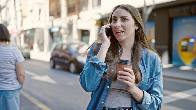 Young beautiful hispanic woman talking on smartphone drinking coffee at street