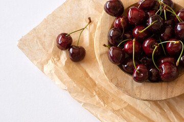 Cherries in a wooden bowl on brown textured paper on a white table