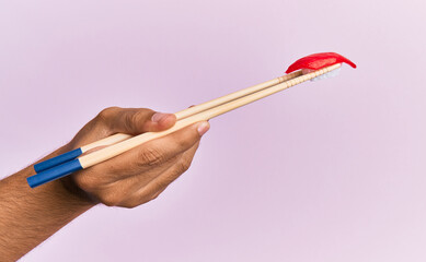  Hand of man holding tuna nigiri with chopsticks over isolated pink background