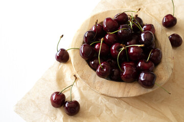 Cherries in a wooden bowl on brown textured paper on a white table with copy space
