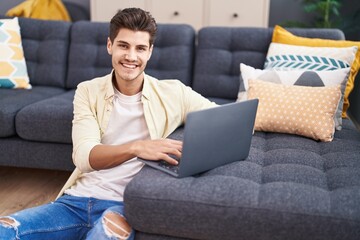 Young hispanic man using laptop sitting on floor at home