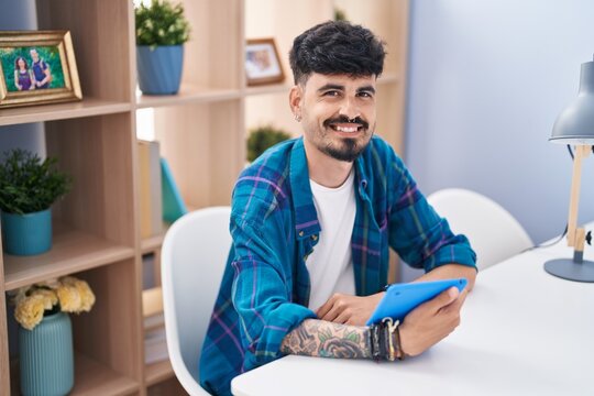 Young hispanic man using touchpad sitting on table at home