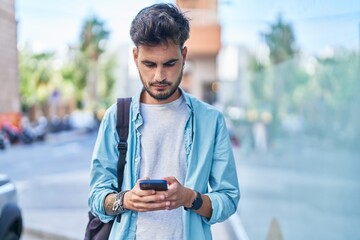 Young hispanic man student using smartphone with relaxed expression at street