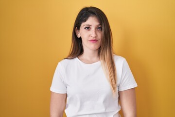 Fototapeta premium Young brunette woman standing over yellow background relaxed with serious expression on face. simple and natural looking at the camera.