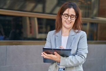 Young woman business worker smiling confident writing on document at street