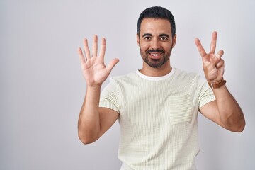 Fototapeta premium Hispanic man with beard standing over isolated background showing and pointing up with fingers number seven while smiling confident and happy.