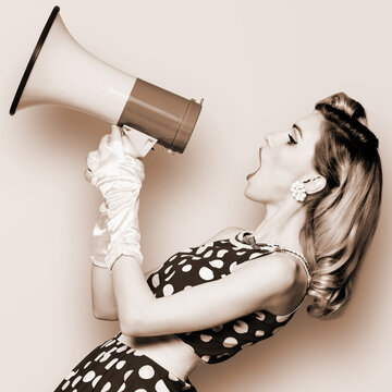 Woman hold mega phone megaphone, shout advertising offer. Girl wear pin up style dress in polka dot yelling loudspeaker. Brown toned monochrome b&w photo. Female model in retro vintage studio photo