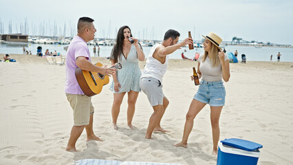 Group of people playing guitar drinking beer dancing at beach