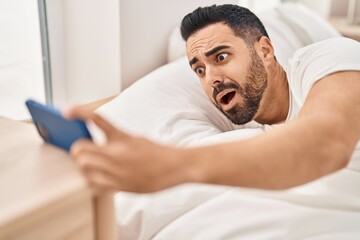 Young hispanic man waking up for alarm smartphone at bedroom