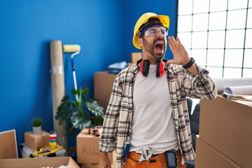 Young hispanic man with beard working at home renovation shouting and screaming loud to side with hand on mouth. communication concept.