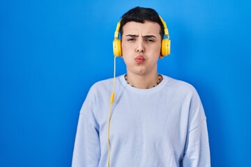 Non binary person listening to music using headphones puffing cheeks with funny face. mouth inflated with air, crazy expression. - obrazy, fototapety, plakaty