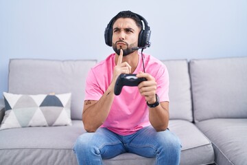Hispanic young man playing video game holding controller sitting on the sofa thinking concentrated about doubt with finger on chin and looking up wondering © Krakenimages.com