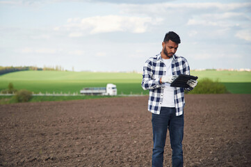 Black colored digital tablet in hands. On the cultivated agricultural field. Handsome Indian man