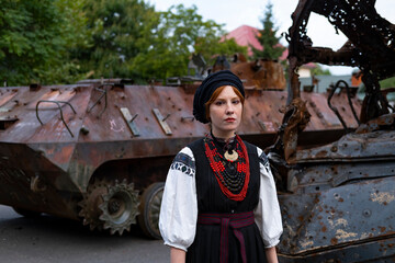 А woman in Ukrainian national embroidered dress vyshyvanka near destroyed russian tank and cars. - 619777776