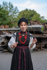 А woman in Ukrainian national embroidered dress vyshyvanka near destroyed russian tank and cars. - 619777799