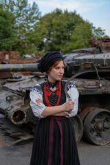 А woman in Ukrainian national embroidered dress vyshyvanka near destroyed russian tank and cars. - 619777903