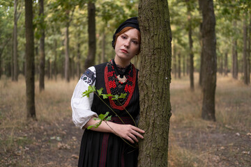 А woman in Ukrainian national embroidered dress vyshyvanka, outdoors in the forest. - 619778112