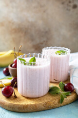 Smoothies with sweet cherry and banana with yogurt on wooden board on a stone background. Fresh seasonal smoothies. Copy space.