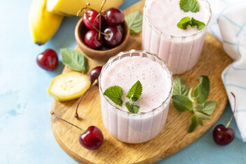 Smoothies with sweet cherry and banana with yogurt on wooden board on a stone background. Fresh seasonal smoothies. Copy space.