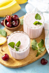 Smoothies with sweet cherry and banana with yogurt on wooden board on a stone background. Fresh seasonal smoothies.