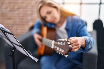 Young blonde woman musician playing classical guitar at music studio