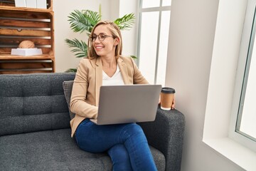 Young blonde woman psychologist using laptop drinking coffee at psychology clinic