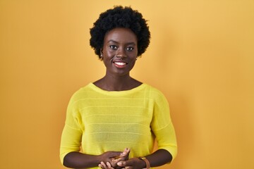 Fototapeta na wymiar African young woman standing over yellow studio with hands together and crossed fingers smiling relaxed and cheerful. success and optimistic