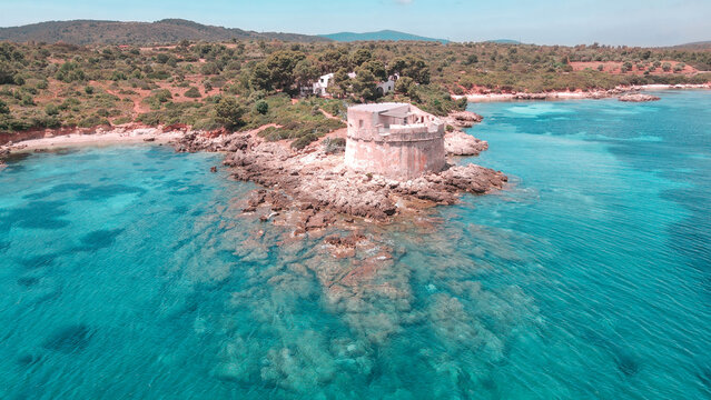 Veduta aerea con il drone della Torre del Lazzaretto di Alghero, circondata da mare blu cristallino e immersa nelle suggestive scogliere