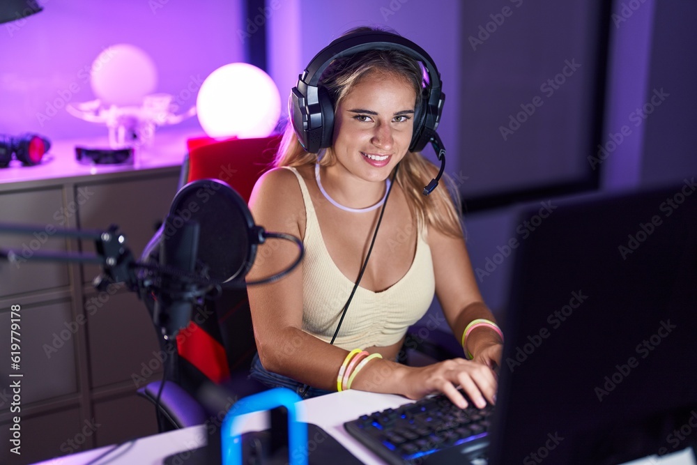 Wall mural young blonde woman streamer playing video game using computer at gaming room