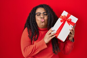 Plus size hispanic woman holding gift looking at the camera blowing a kiss being lovely and sexy. love expression.